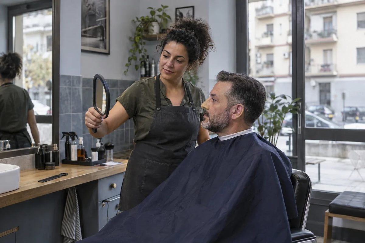 Una professionista e un cliente osservano il taglio con uno specchio a mano in barberia.