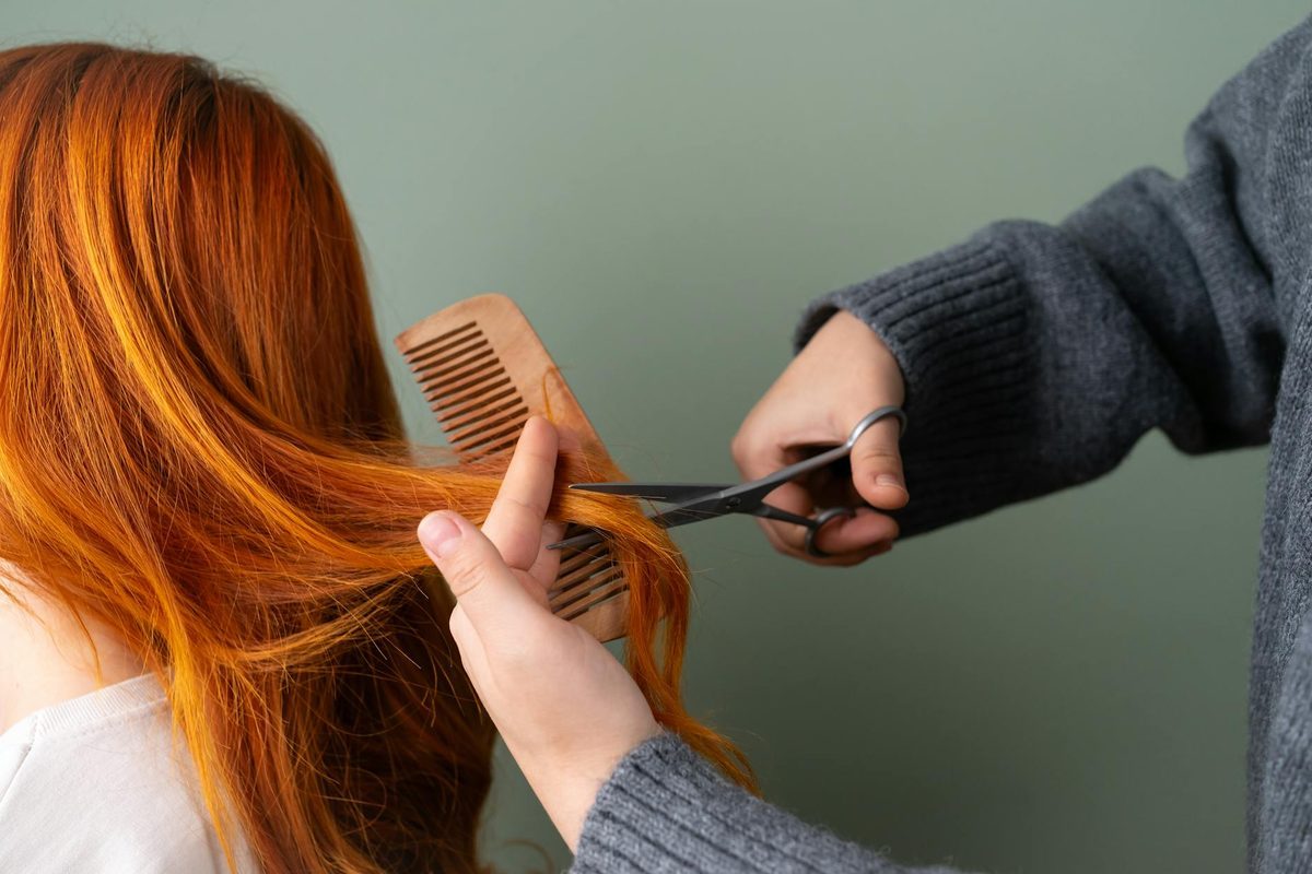 Parrucchiera che taglia le punte di capelli ramati con forbici e pettine in legno